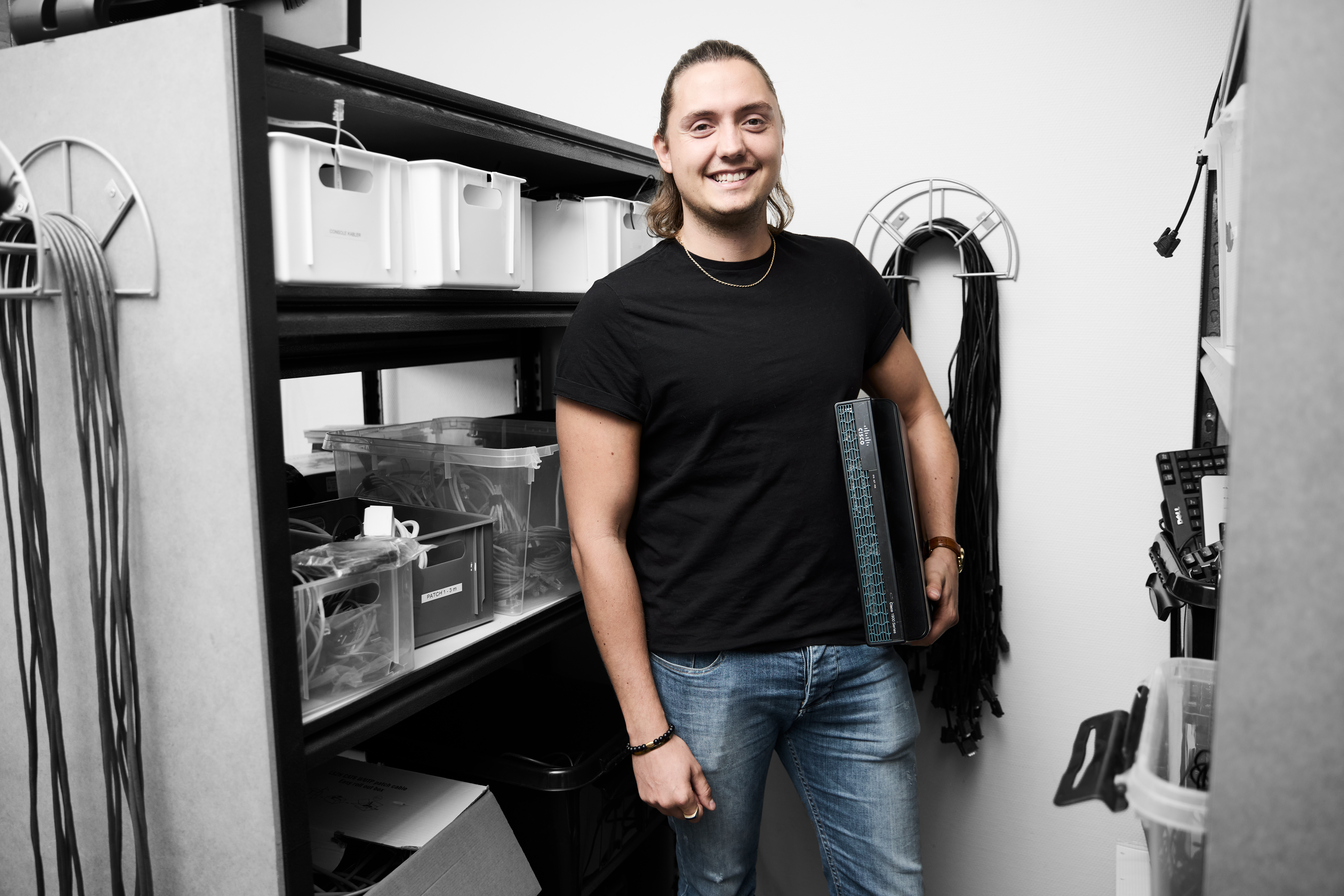 Datateknikker smiler, mens han står med en computer undr armen