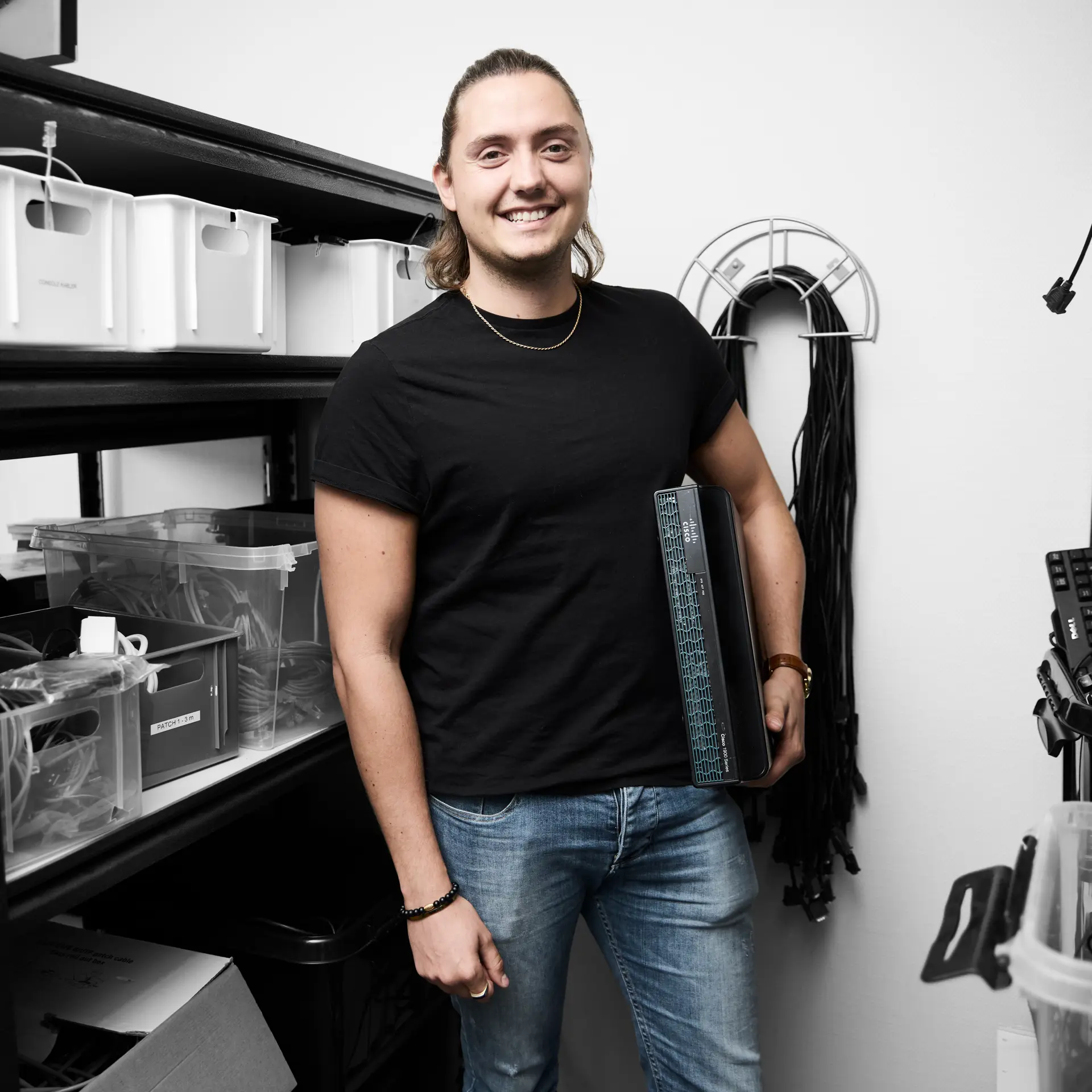 Datateknikker smiler, mens han står med en computer undr armen
