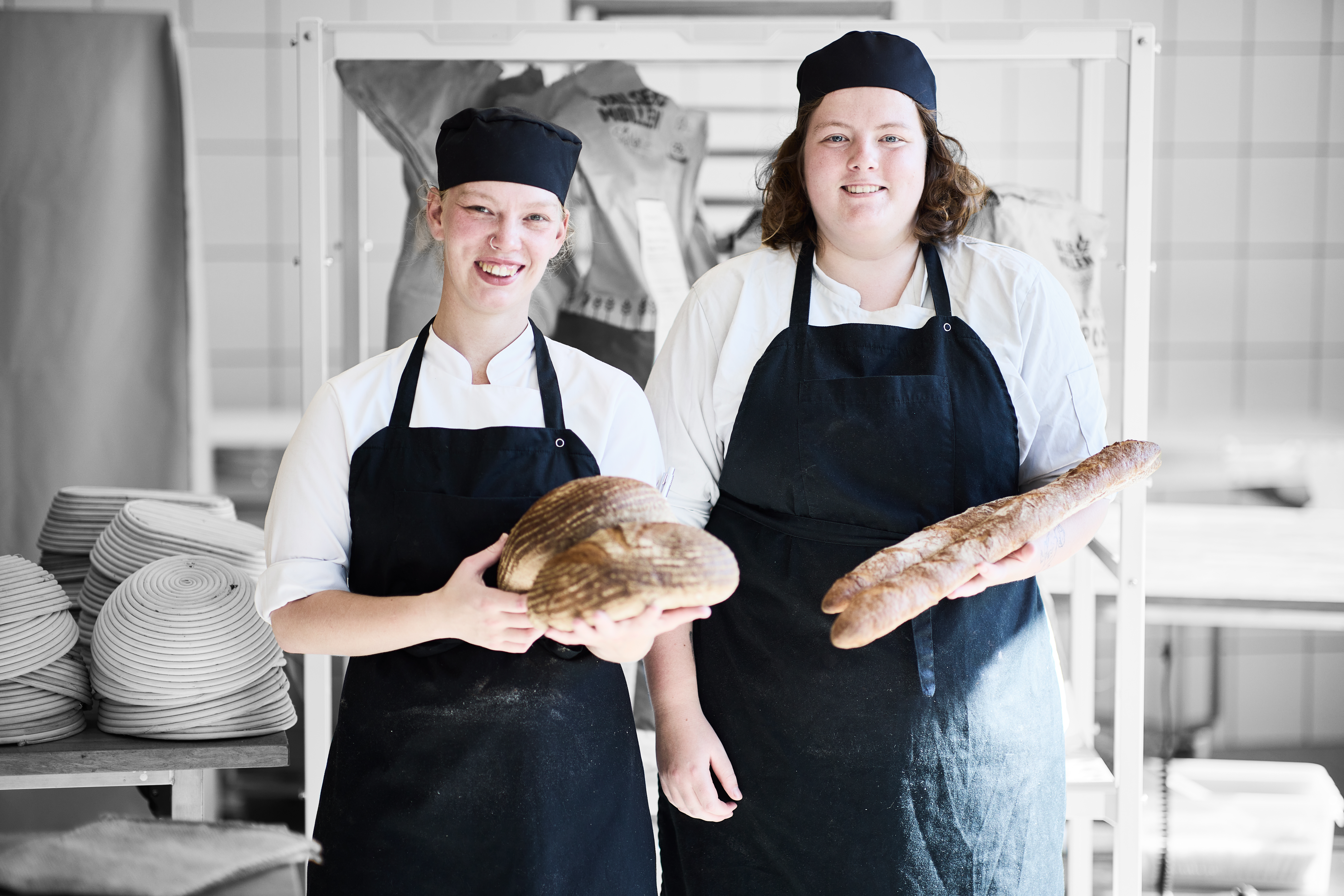 Bagere står med brød i hånden i et køkken