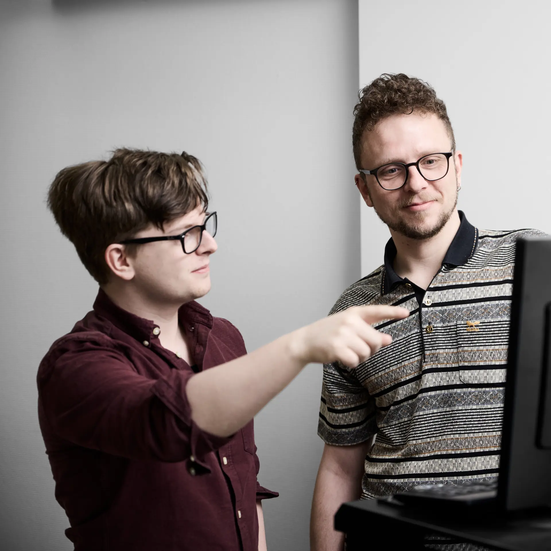 Datateknikere står ved en computer, mens den ene peger på computerskærmen, og den anden lytter