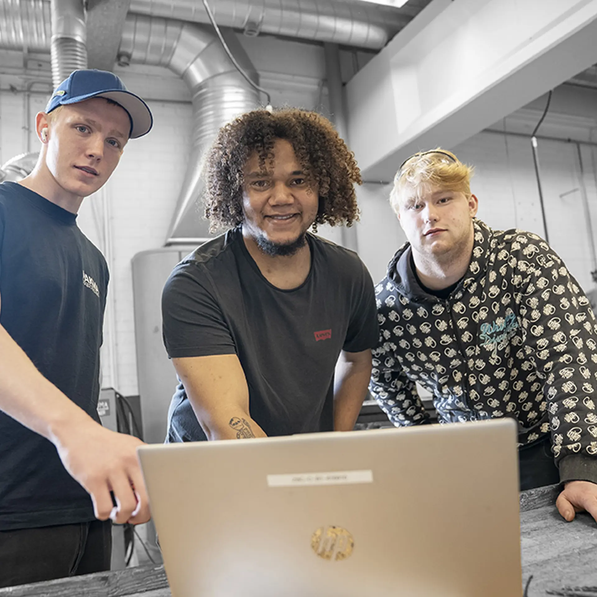 Elever  på industriteknikeruddannelsen står med computer i værkstedet