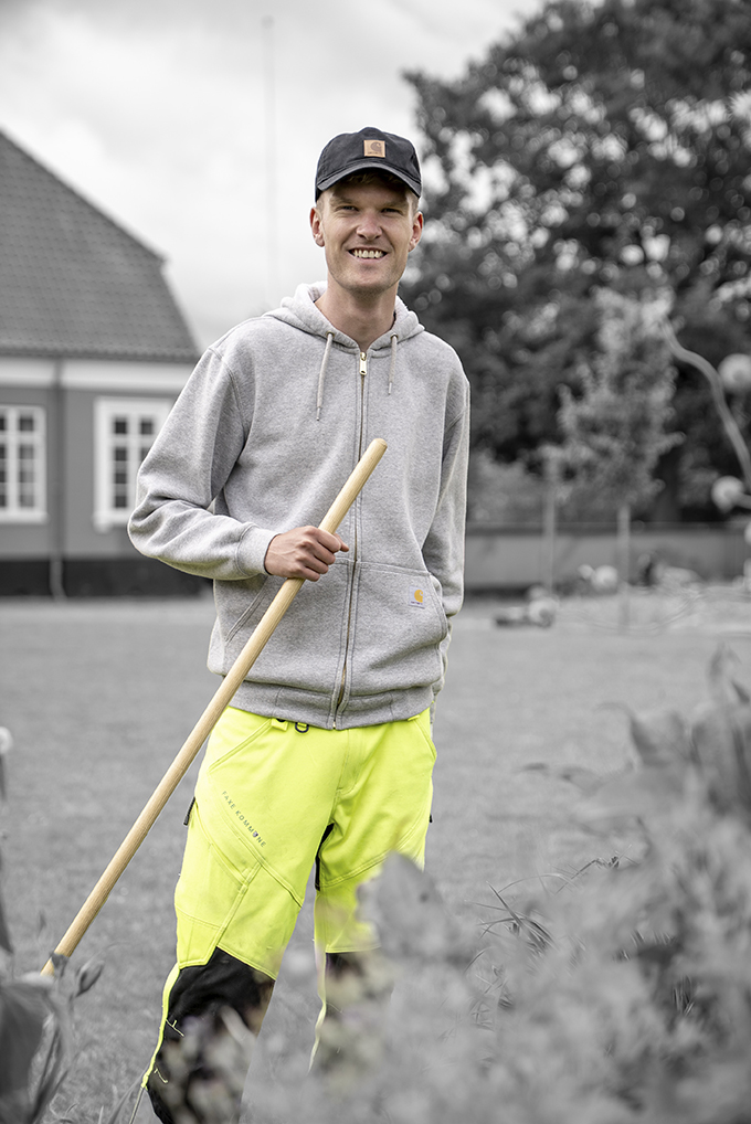 Anlægsgartnerelev med gule arbejdsbukser og rive