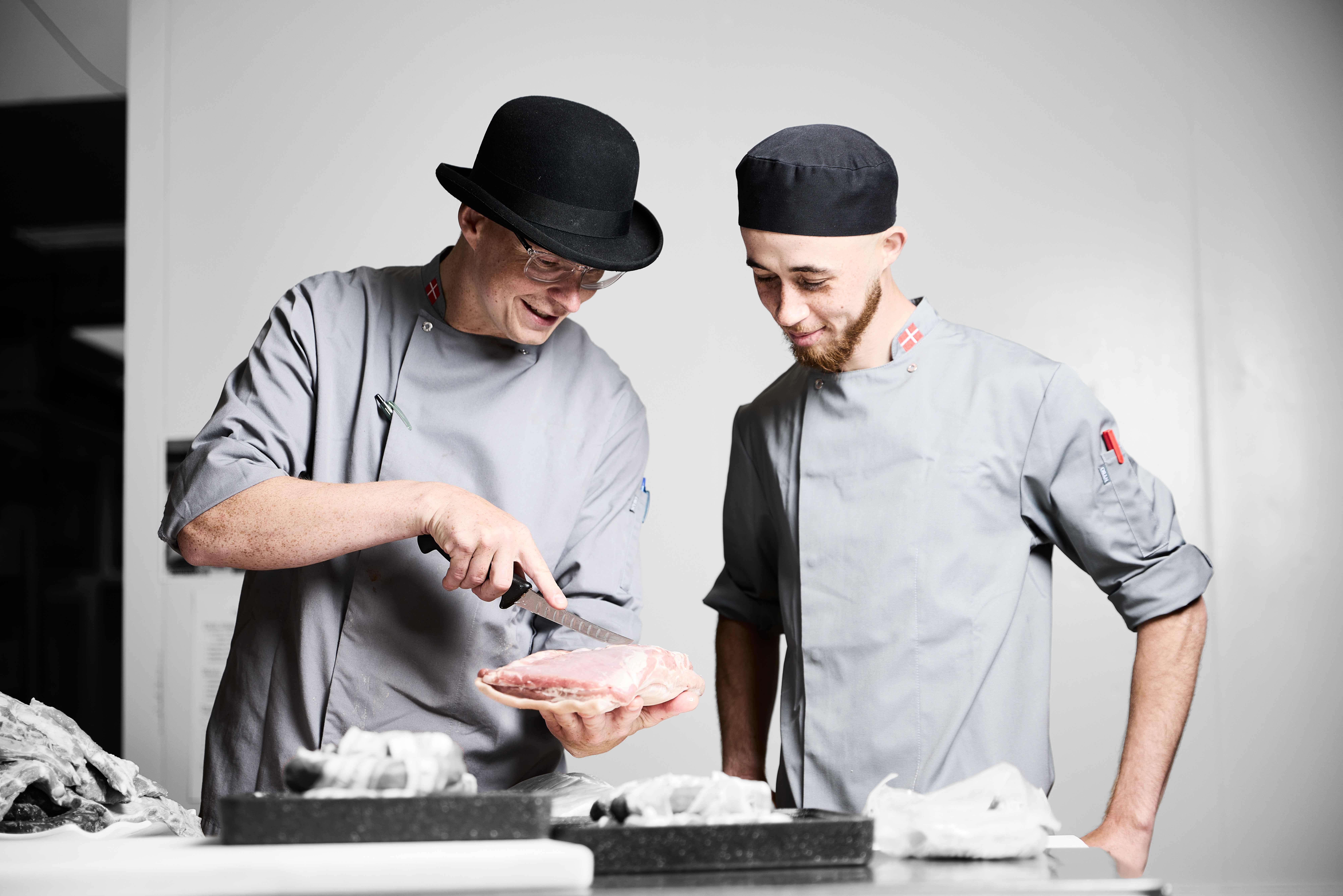 Gourmetslagter får undervisning af sin faglærer, som viser, hvordan et stykke kød skal skæres