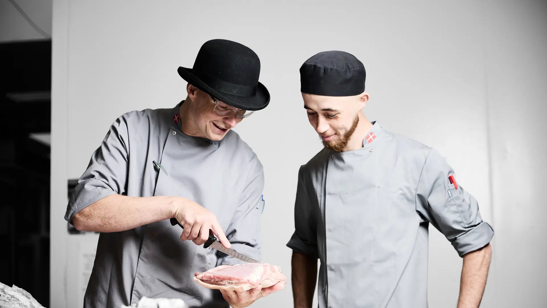 Gourmetslagter får undervisning af sin faglærer, som viser, hvordan et stykke kød skal skæres