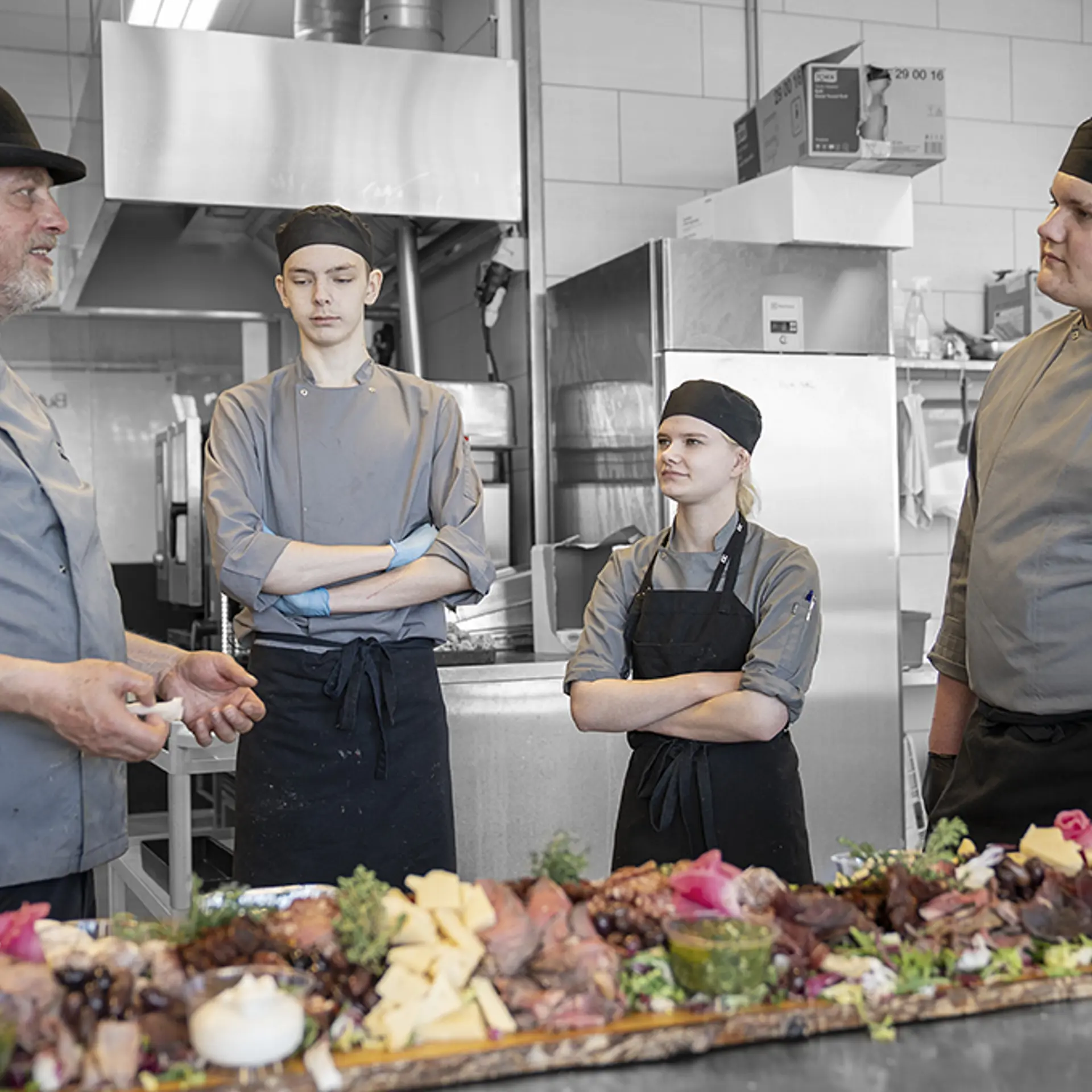 Underviser og elever på gourmetslagteruddannelsen står med smørrebrød i køkkenet