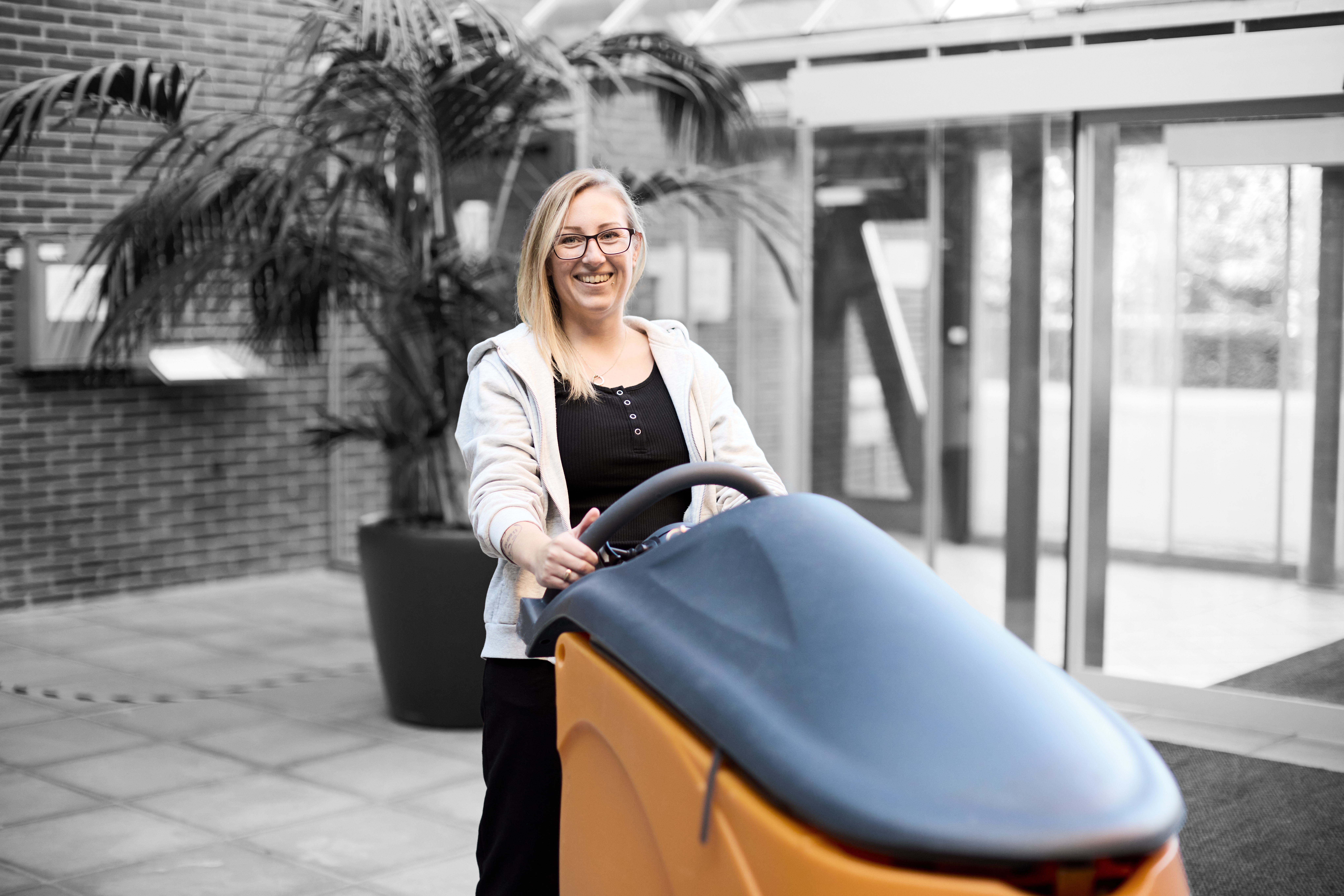 Serviceassistent smiler til kameraet, mens hun står ved en rengøringsvogn