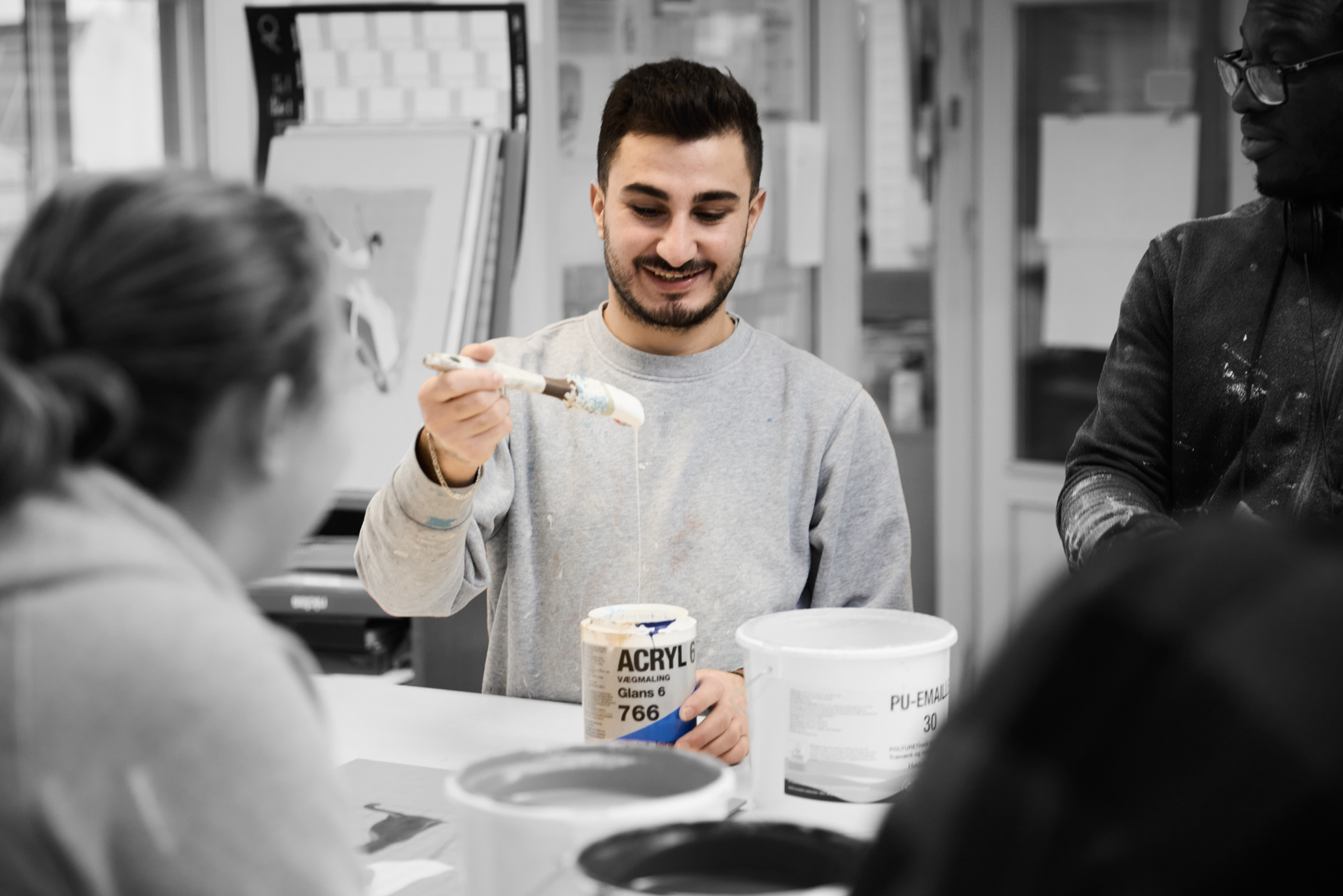 Maler står med acryl maling, mens han står ved en bord sammen med andre elever