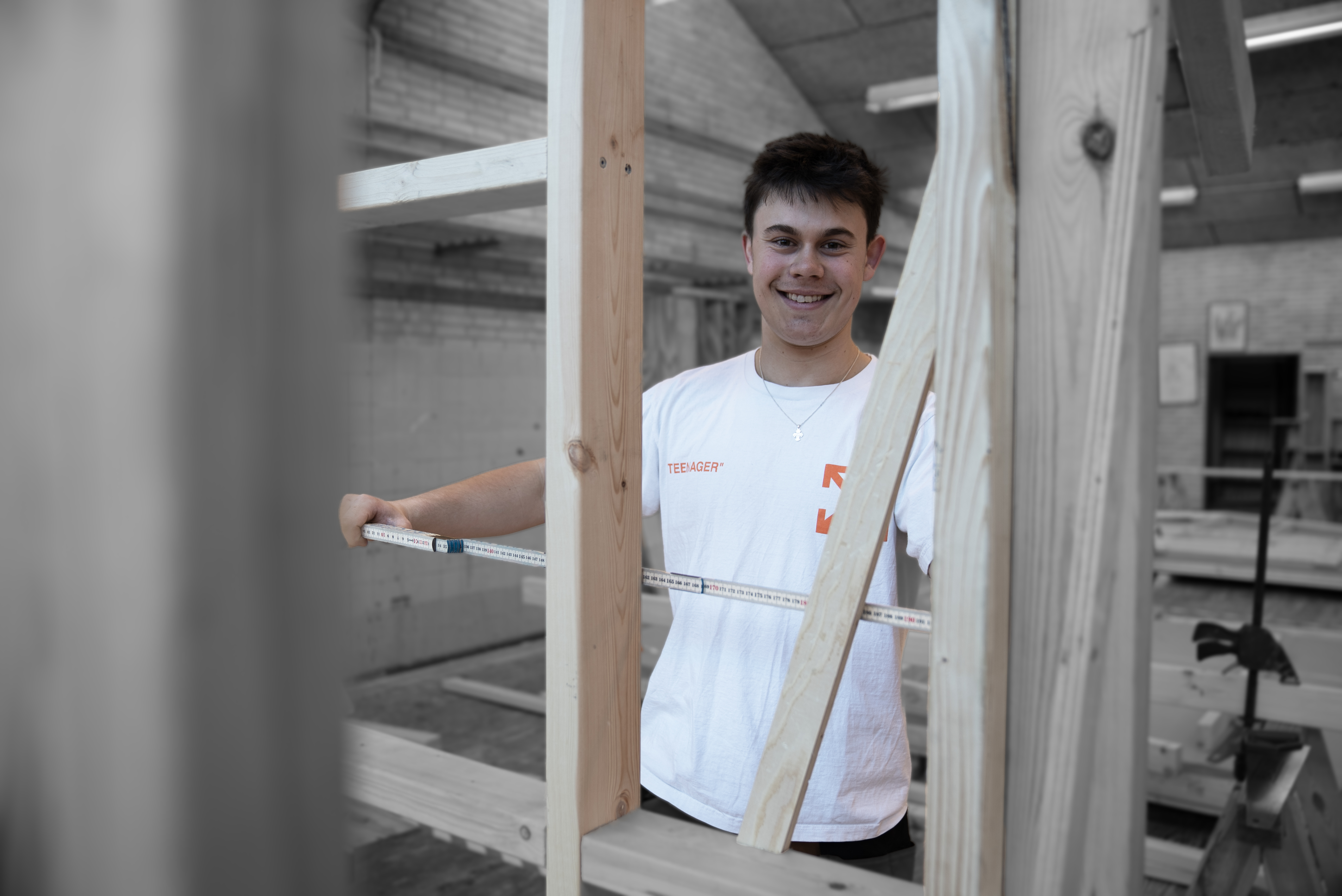 Tømrerelev måler træ og smiler til kamera