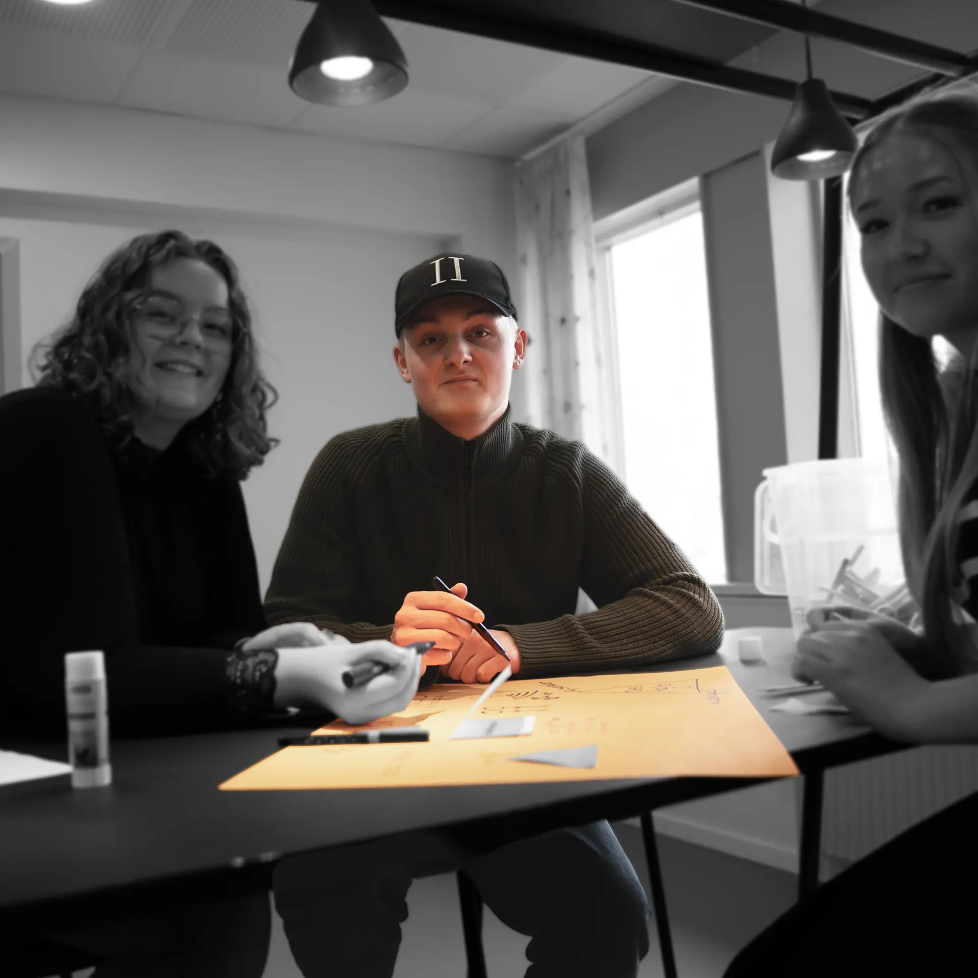 Pædagogisk assistentelever arbejder med opgave og kigger i kamera