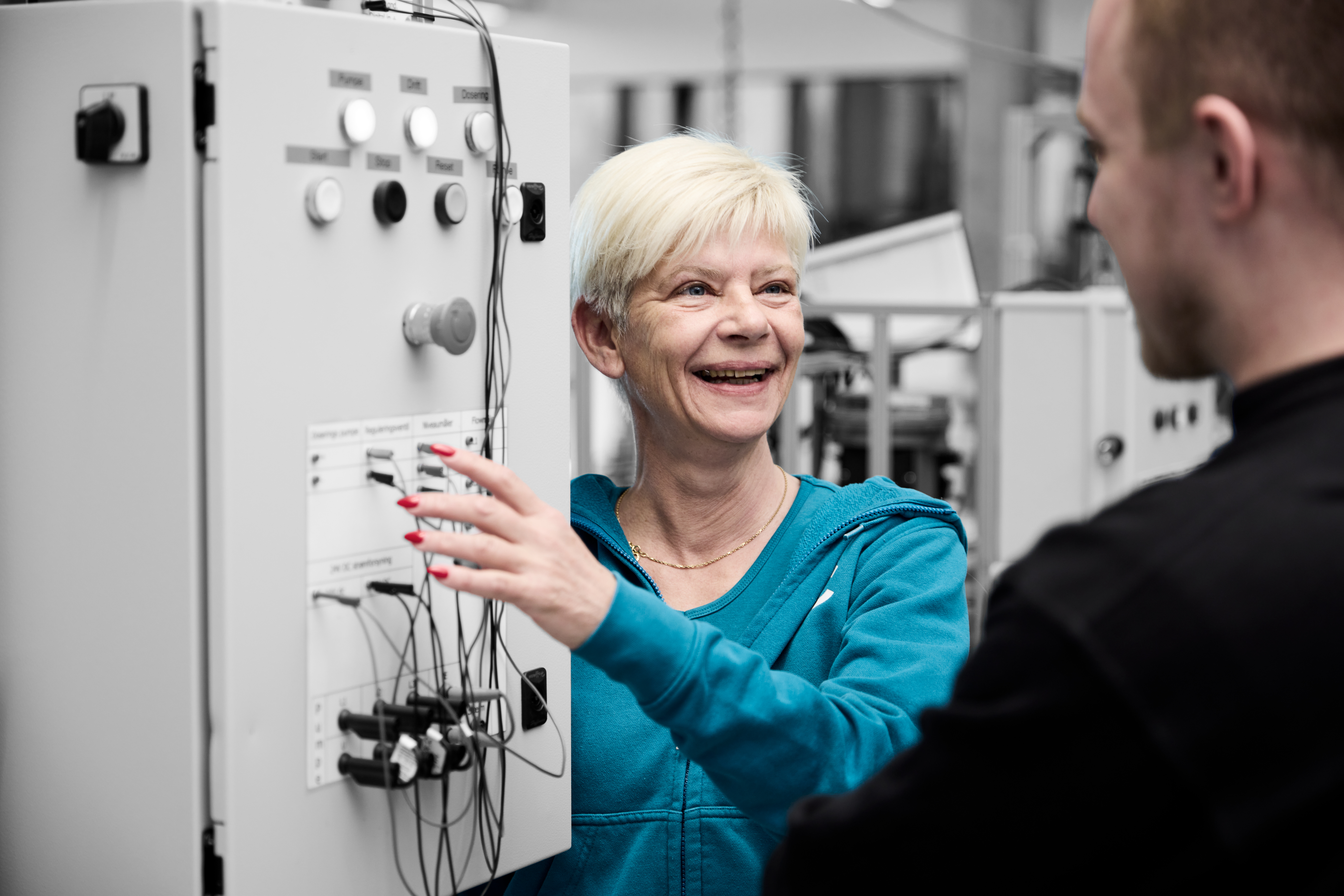 Automatiktekniker smiler til en elev, mens de står ved et anlæg