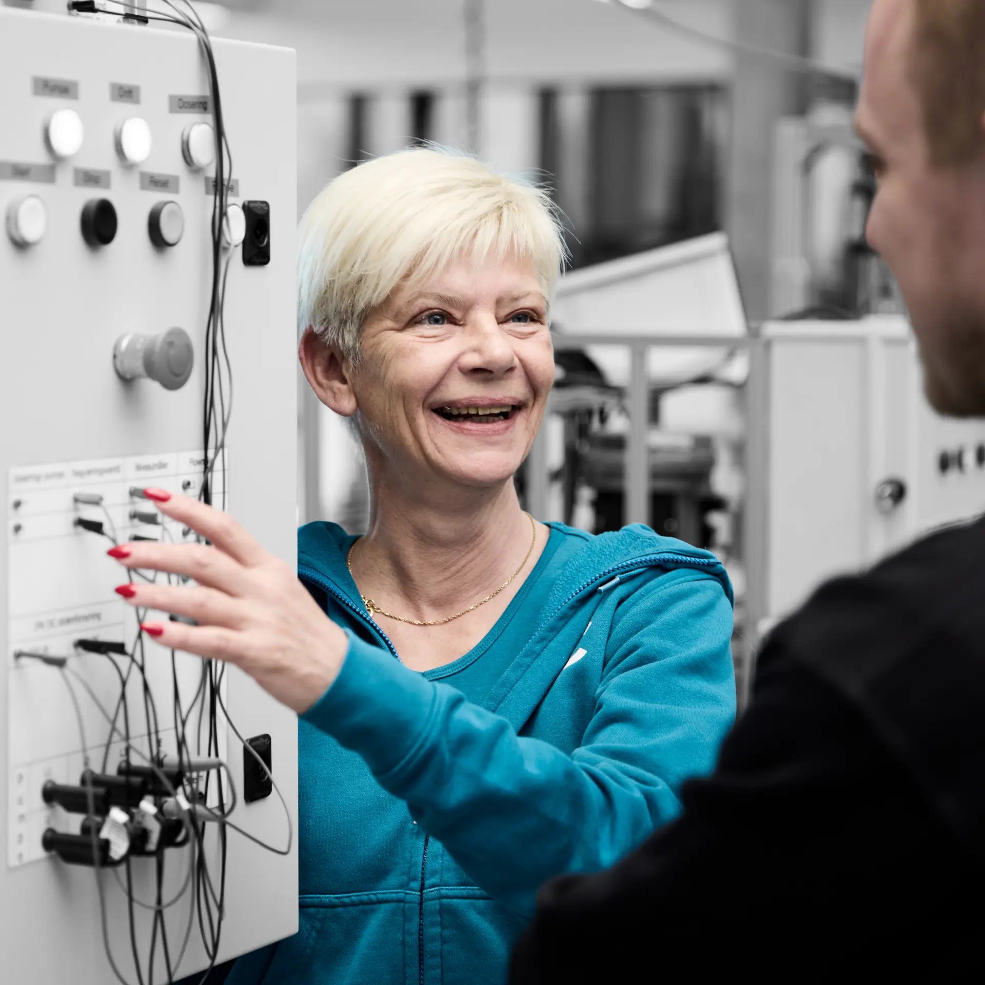 Automatiktekniker smiler til en elev, mens de står ved et anlæg