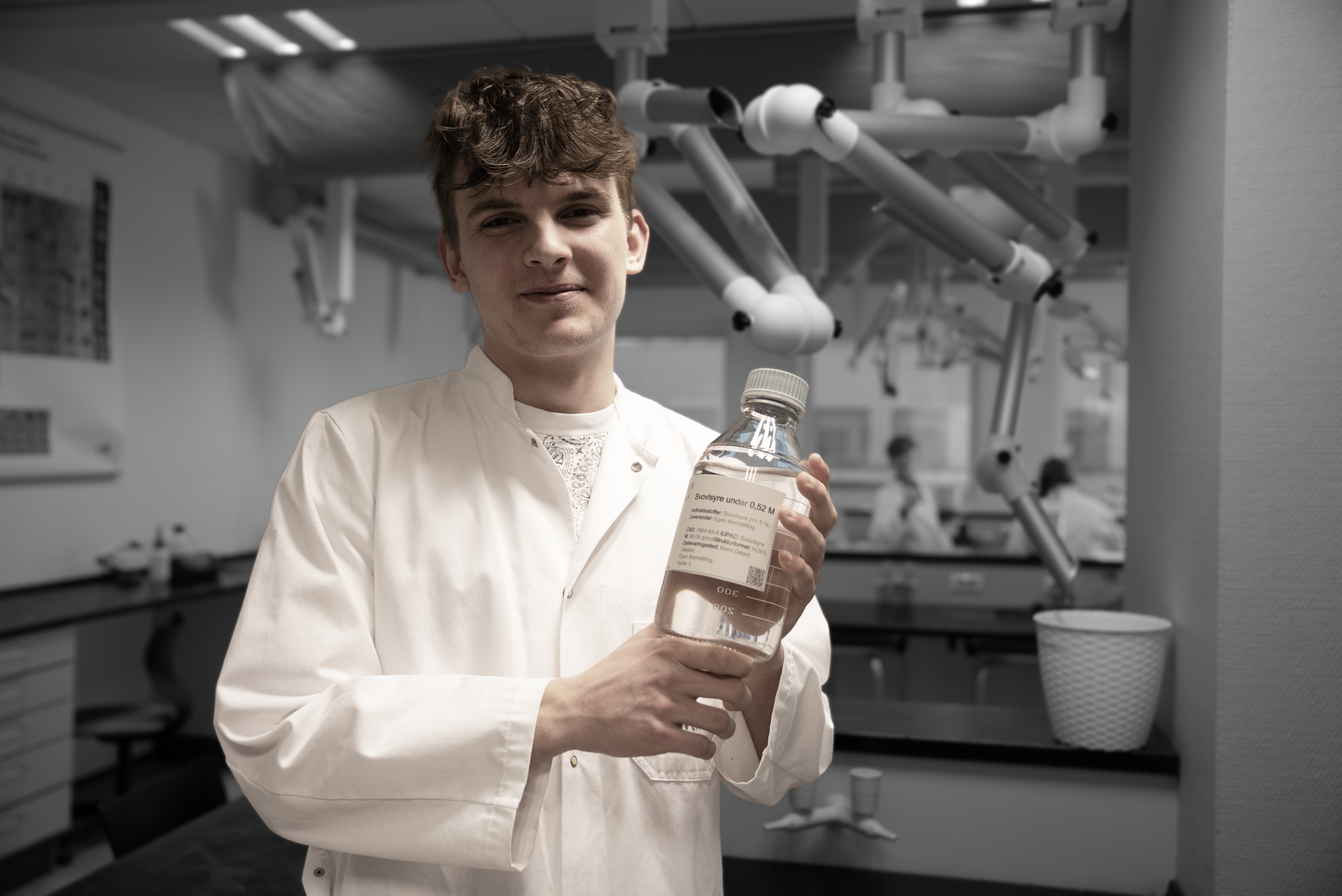 HTX-elev i kittel står med en flaske i hænderne