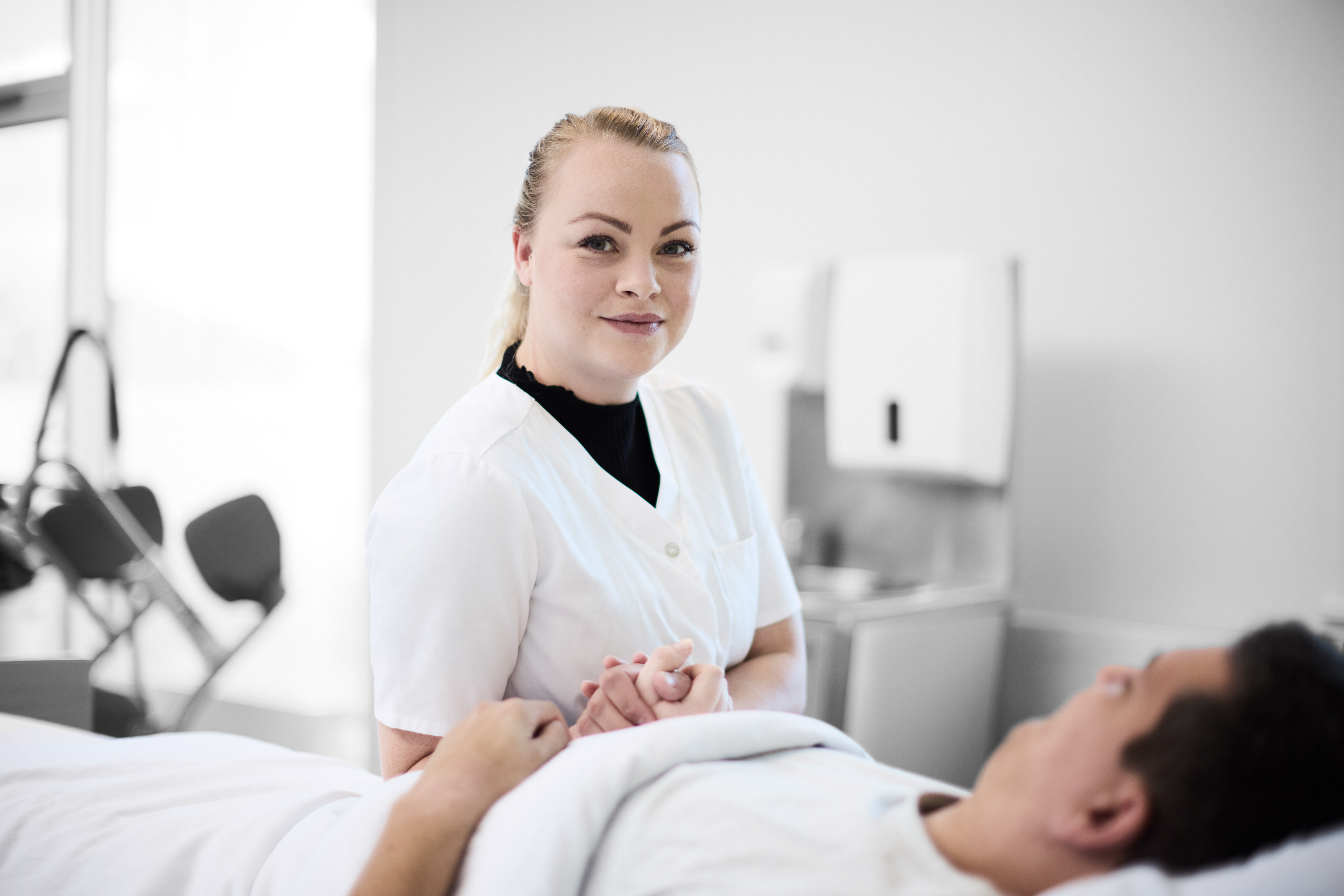 Social- og sundhed: elev sidder i en hospitalseng, hvor hun holder en patient i hånden