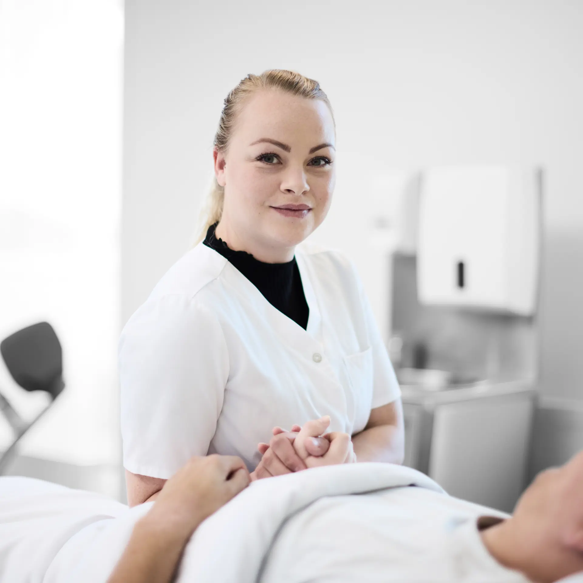 Social- og sundhed: elev sidder i en hospitalseng, hvor hun holder en patient i hånden