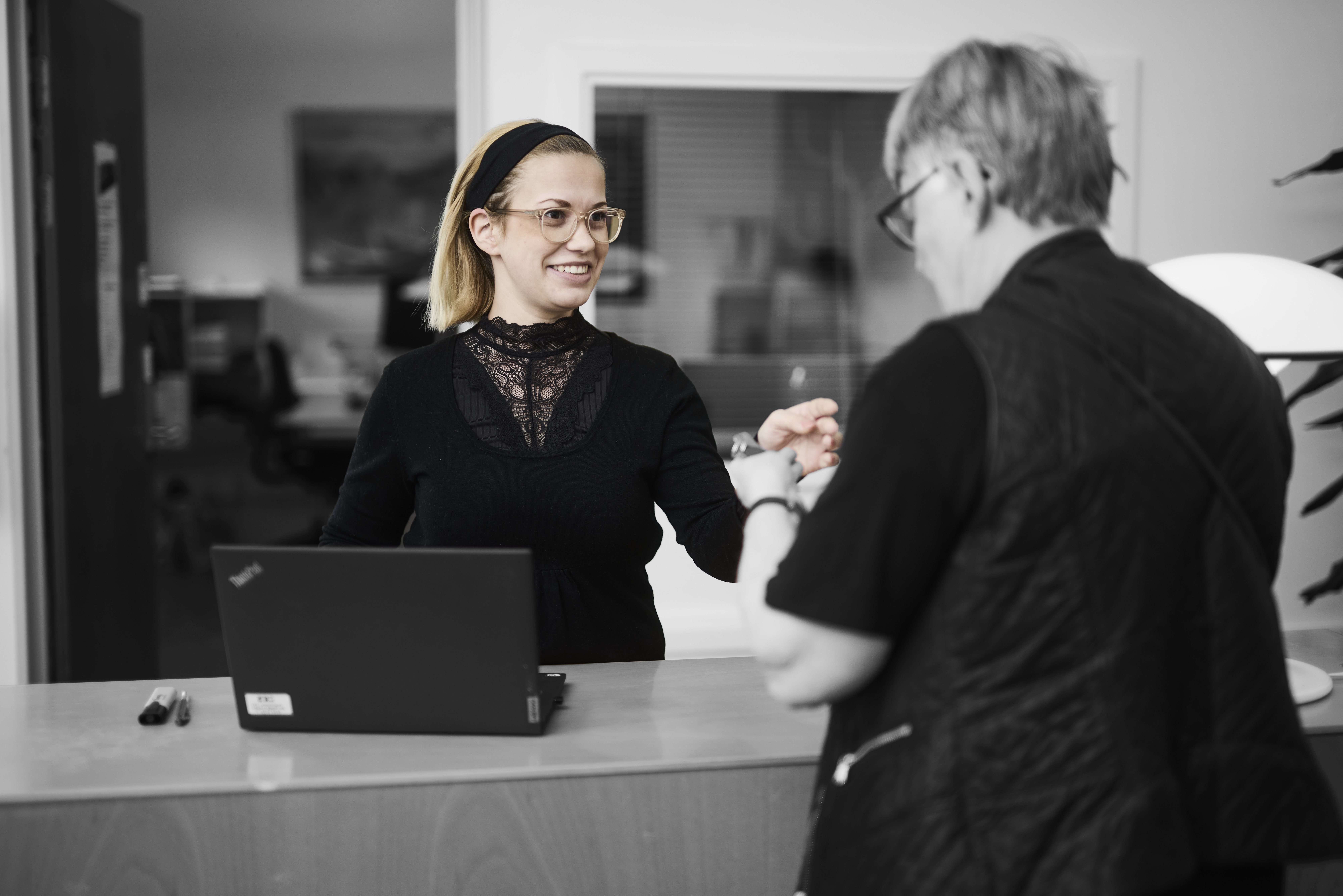 Receptionist står ved skranke og smiler til en kunde, som får udleveret et sæt nøgler