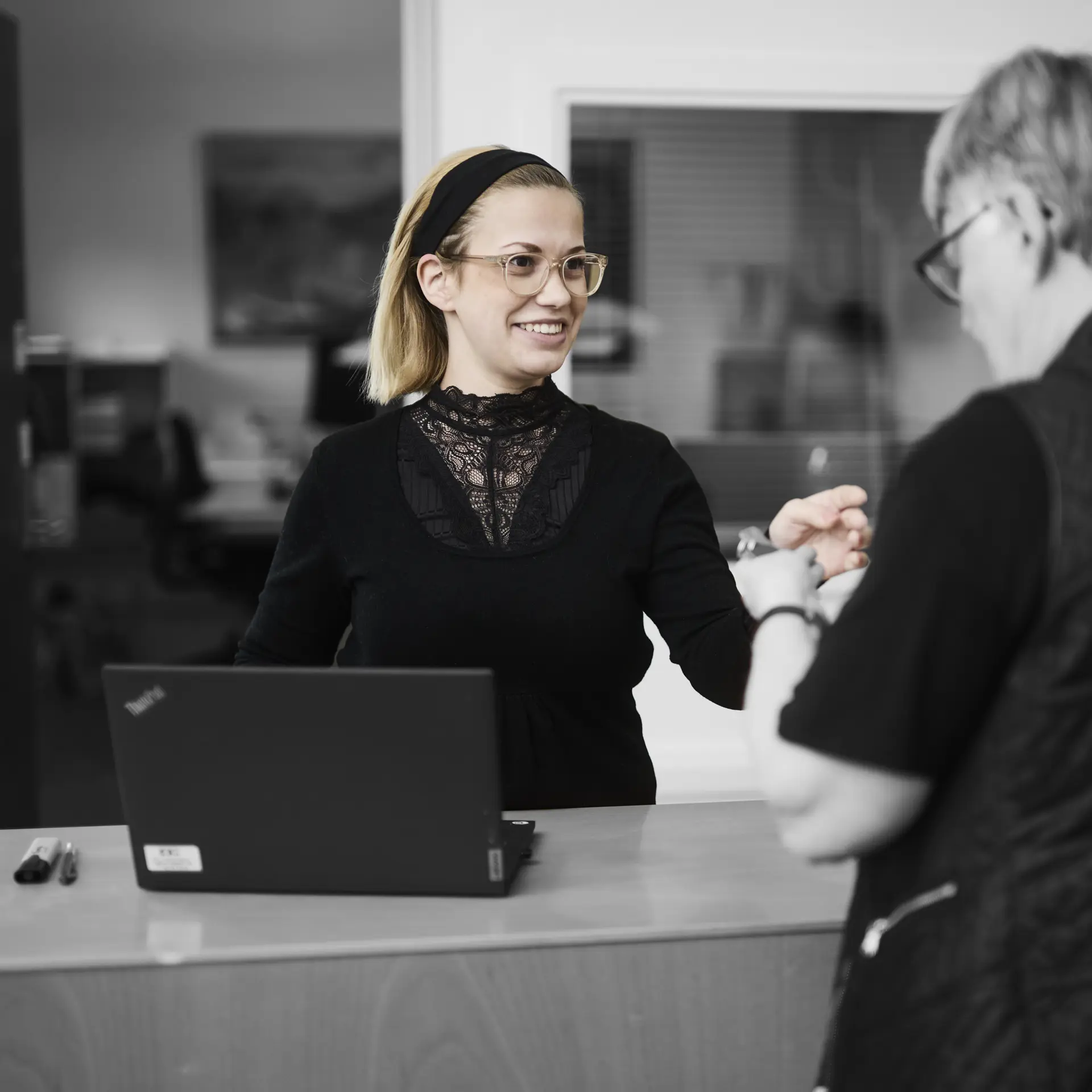 Receptionist står ved skranke og smiler til en kunde, som får udleveret et sæt nøgler