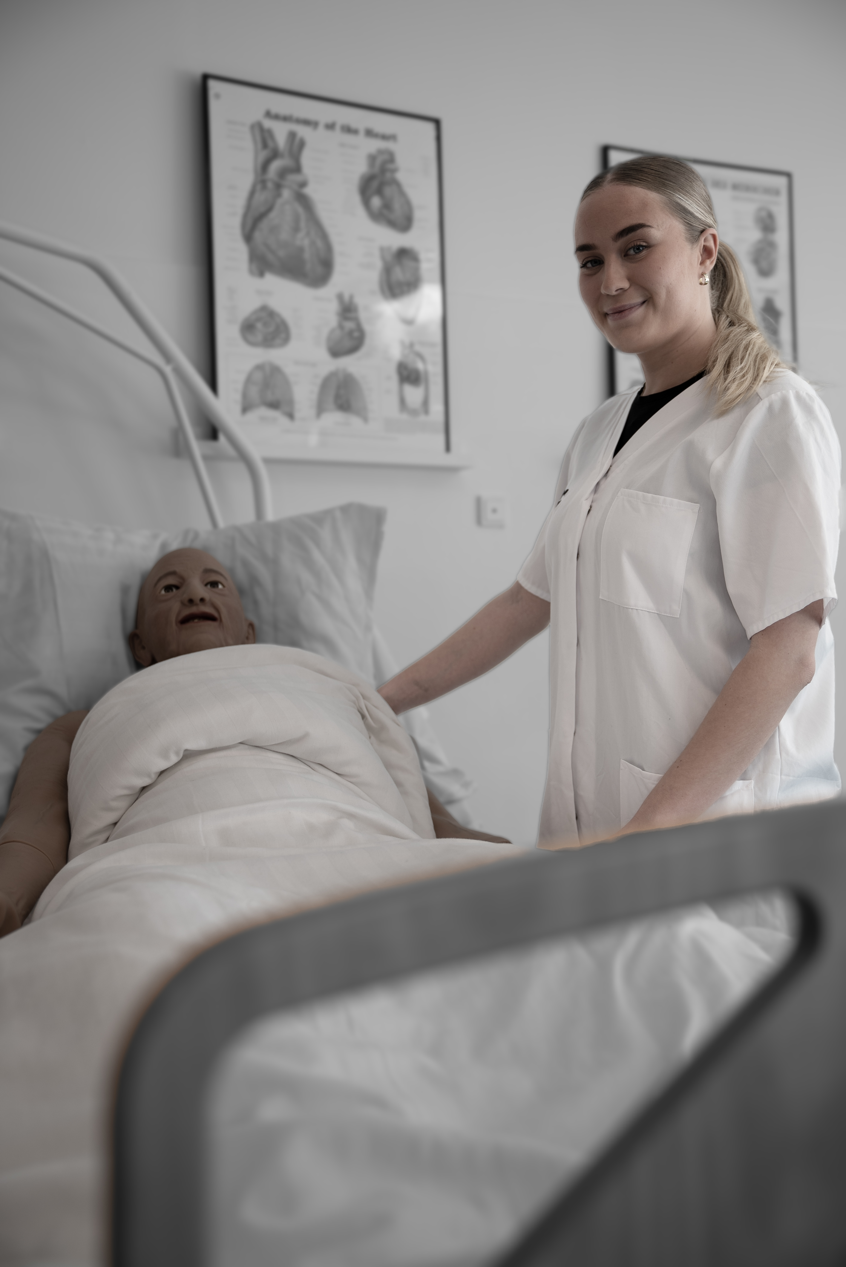 Elev på social- og sundhedsassistentuddannelsen står ved seng med træningsdukke