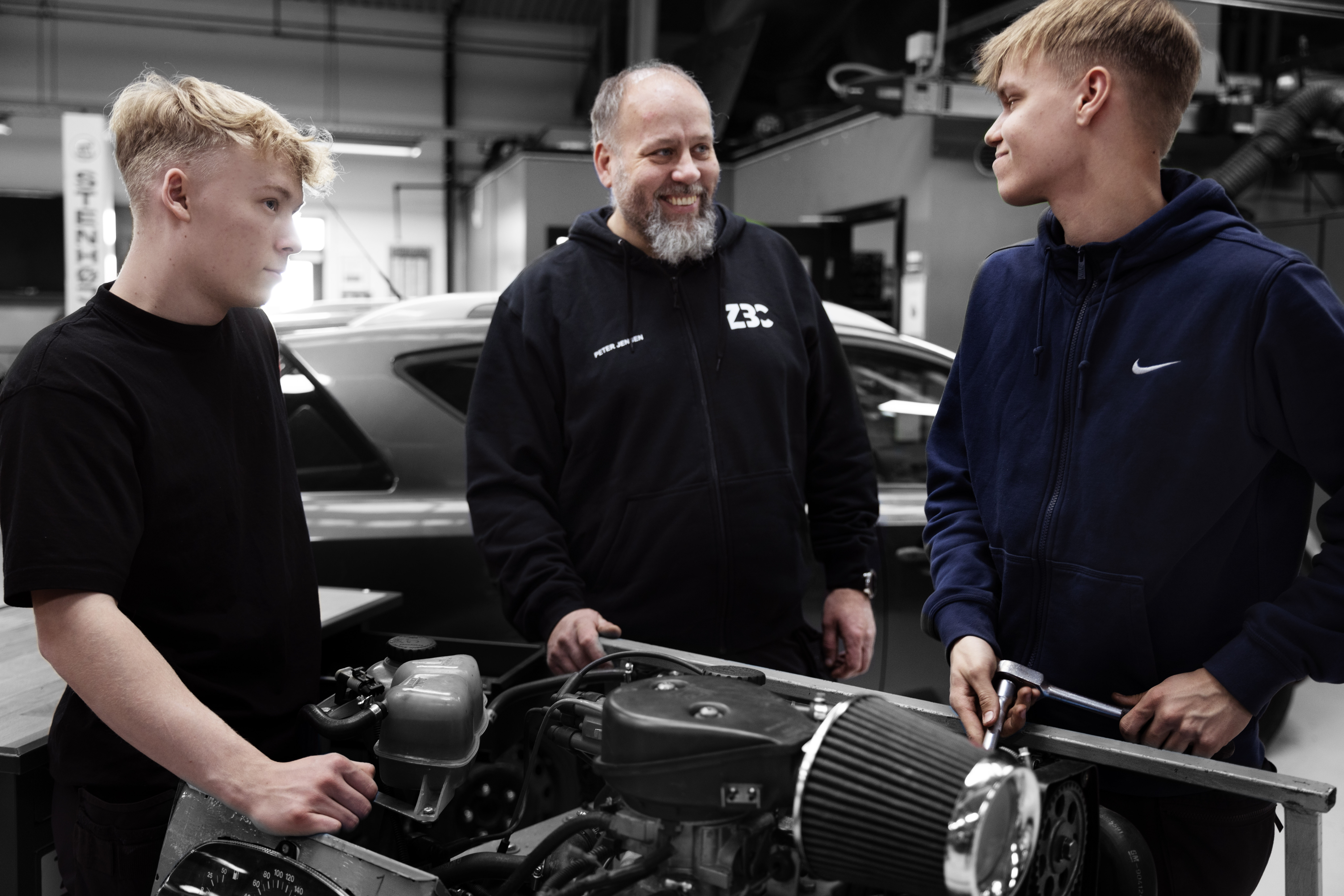 Personvognsmekanikere og faglærer står sammen på værksted