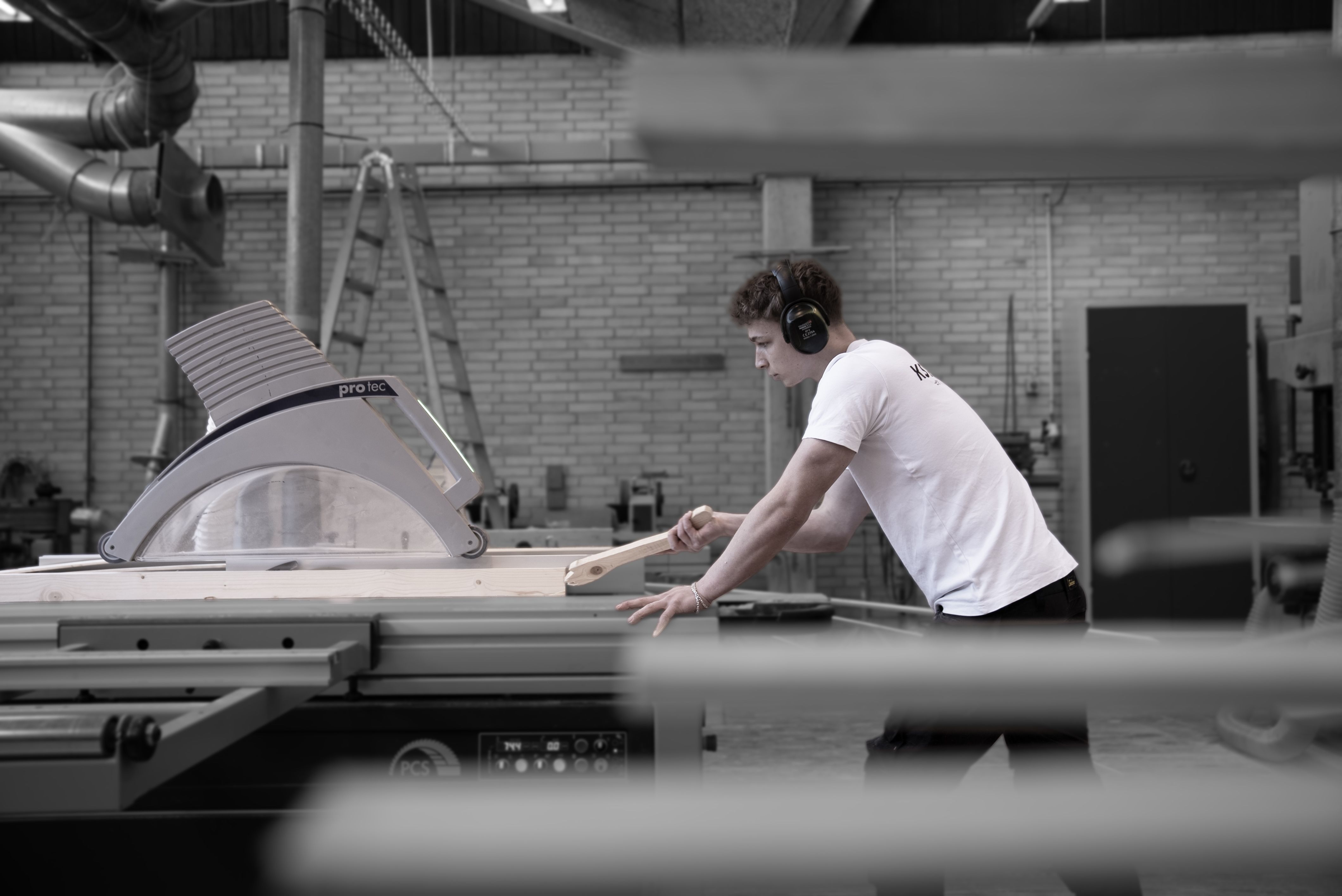 Tømrerelev skærer træ på værksted med maskine