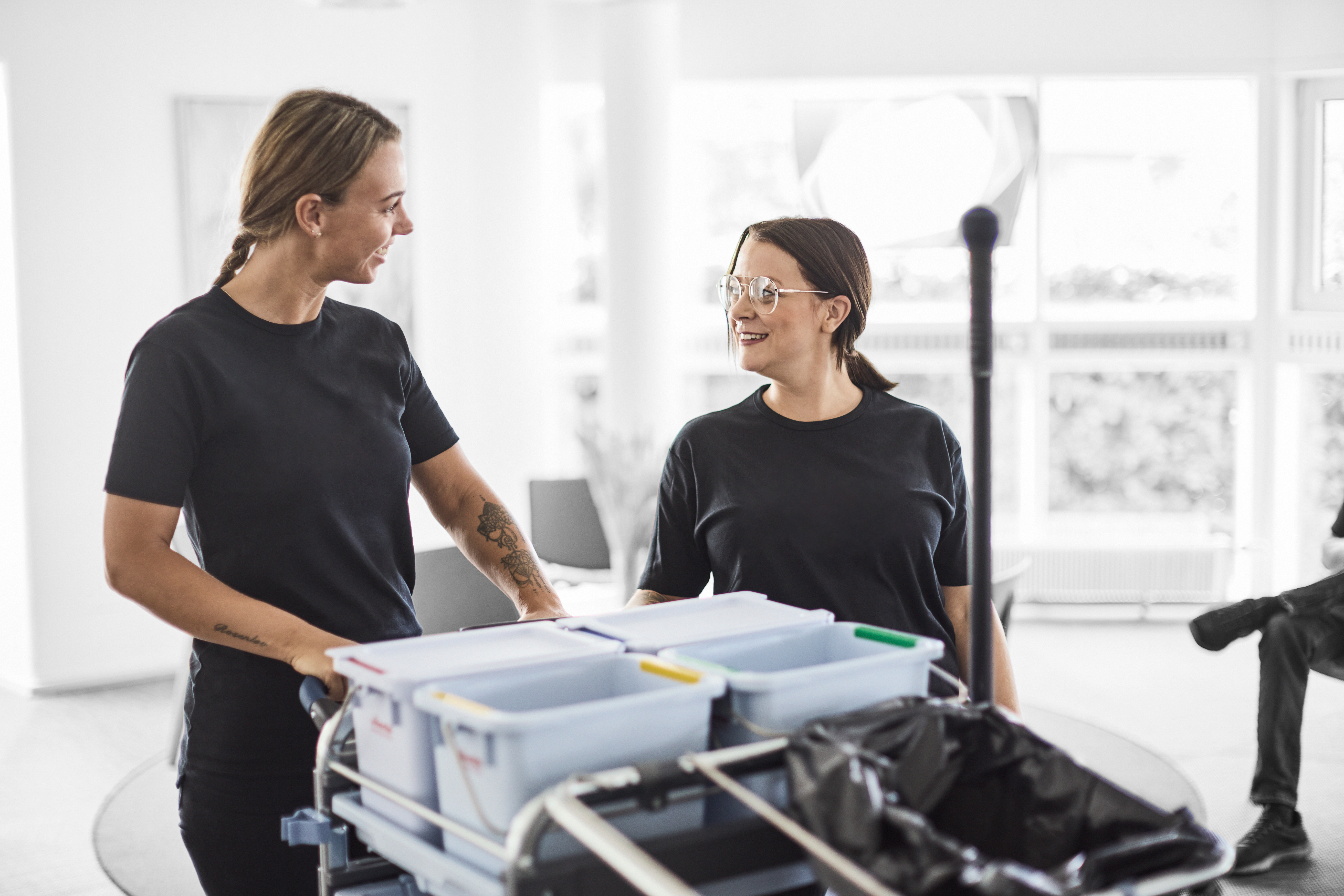 Serviceassistent smiler til hinanden, mens de står ved en rengøringsvogn