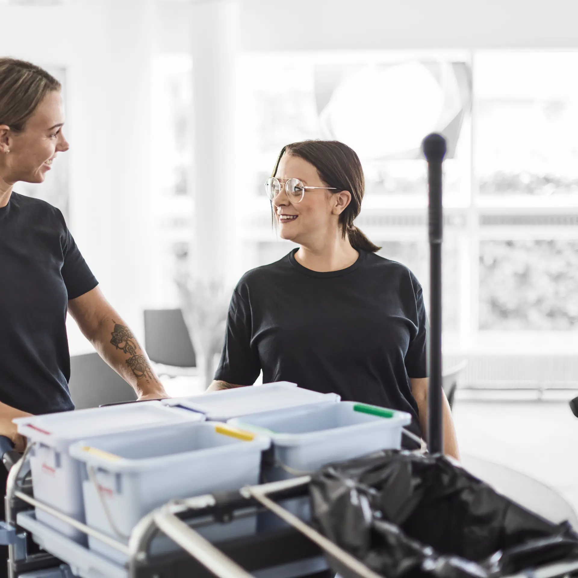 Serviceassistent smiler til hinanden, mens de står ved en rengøringsvogn