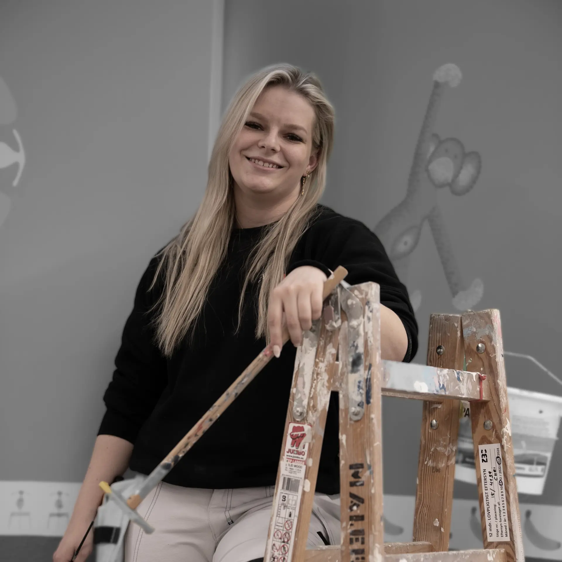 Bygningsmalerelev med stige smiler til kameraet