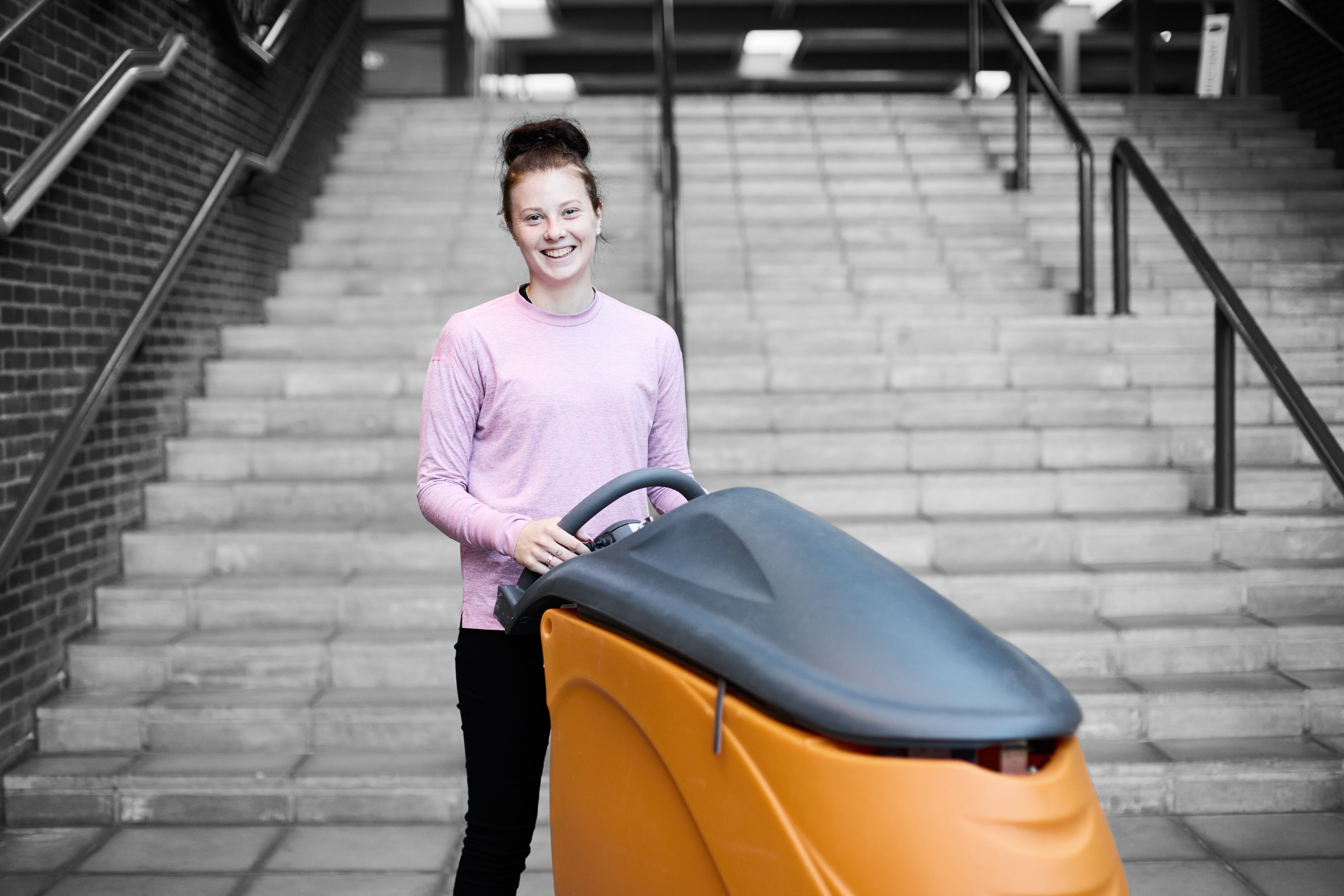 Serviceassistent smiler til kameraet, mens hun står ved en rengøringsvogn