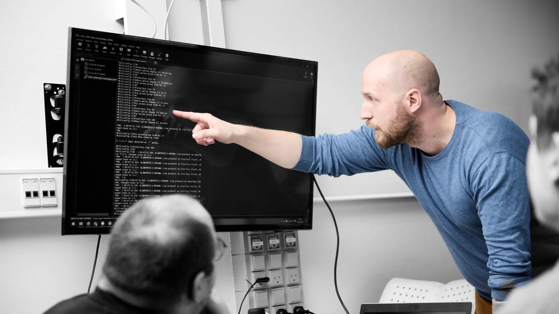 Datatekniker peger på en skærm med en masse koder på, mens andre elever ser på