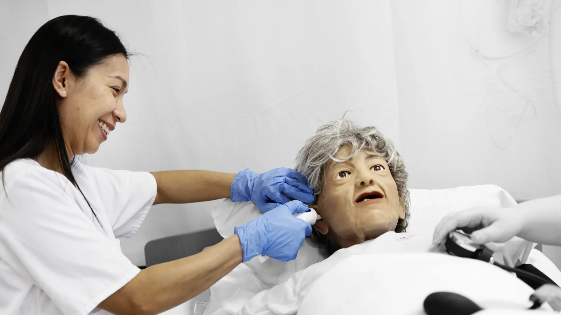 Social- og sundhedsassistent tager temperaturen i øret på en dukke i hospitalsseng