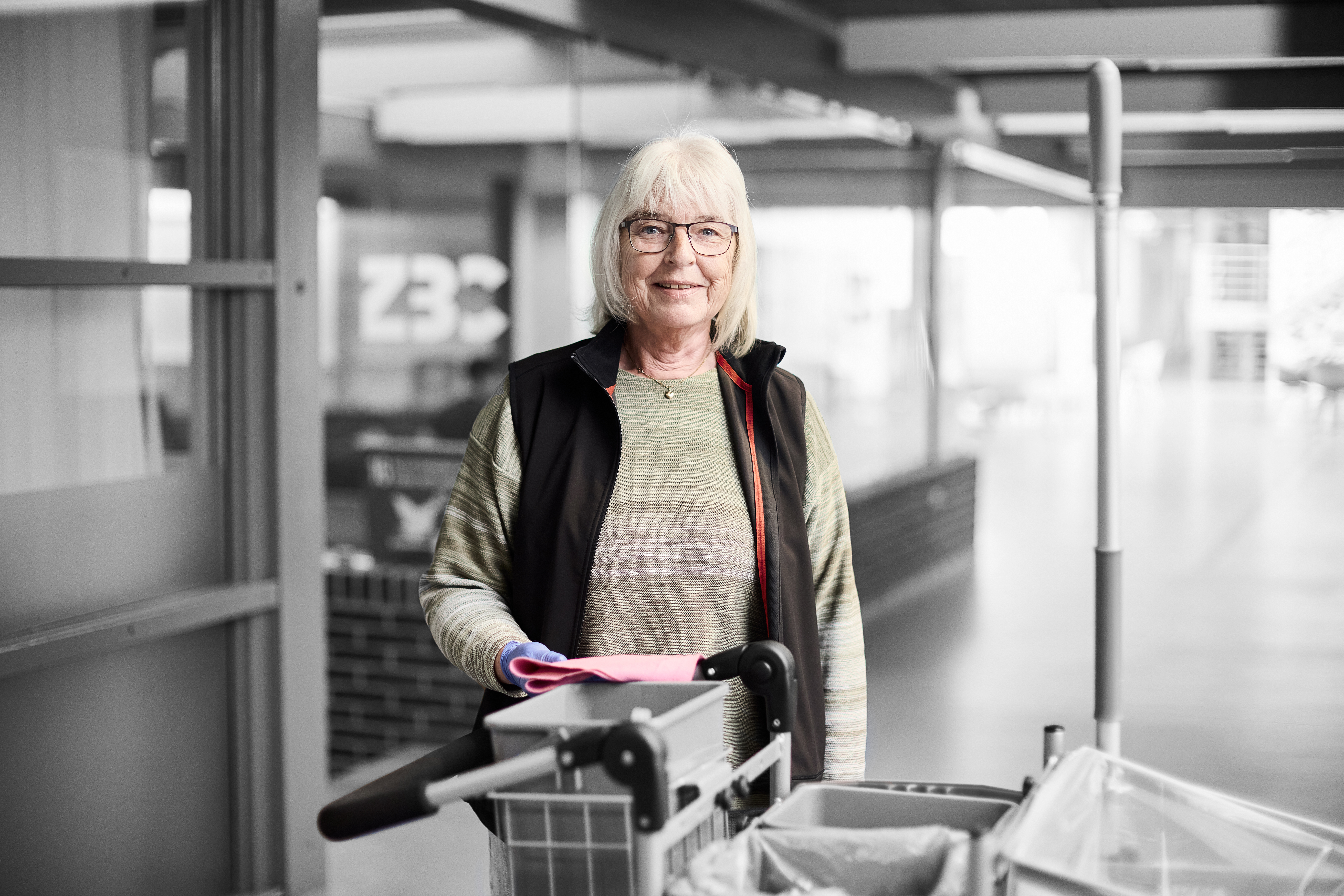 Serviceassistent smiler til kameraet, mens hunstår ved en rengøringsvogn