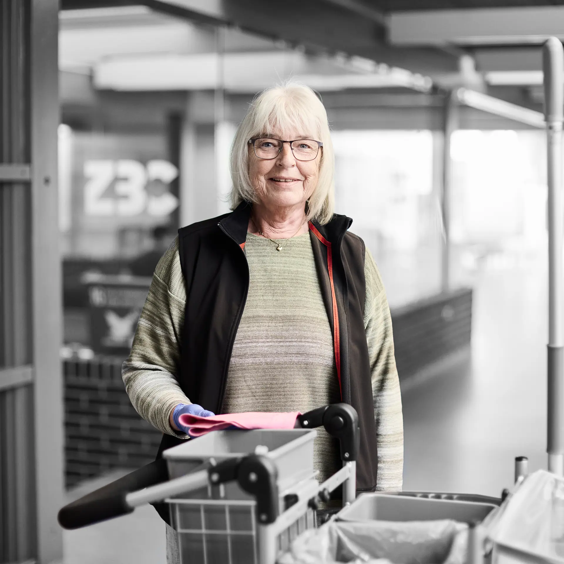 Serviceassistent smiler til kameraet, mens hunstår ved en rengøringsvogn