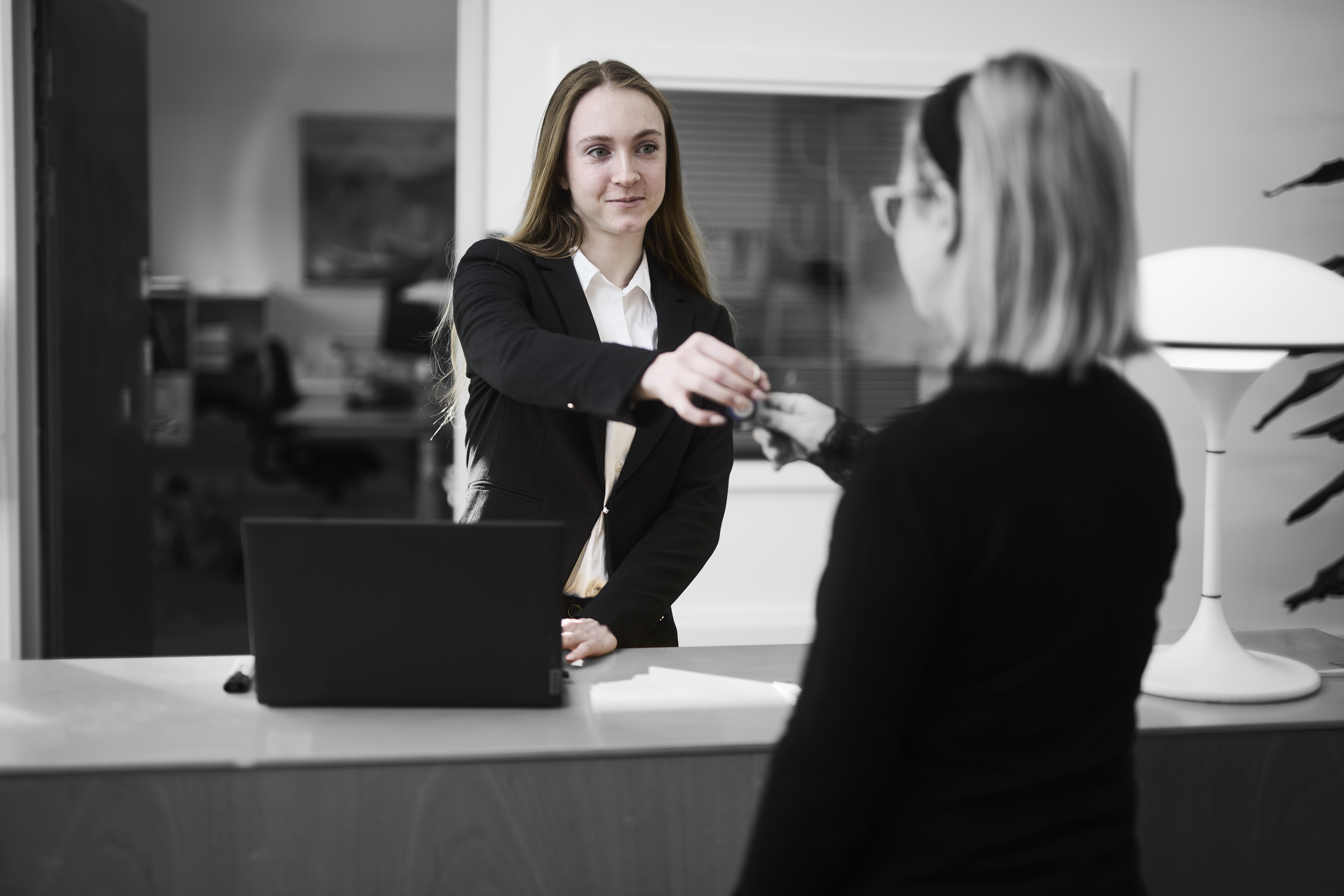 Receptionist står ved en skranke, hvor hun udleverer et sæt nøgler til kunde