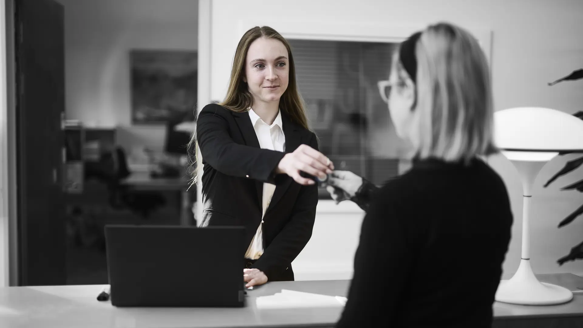 Receptionist står ved en skranke, hvor hun udleverer et sæt nøgler til kunde