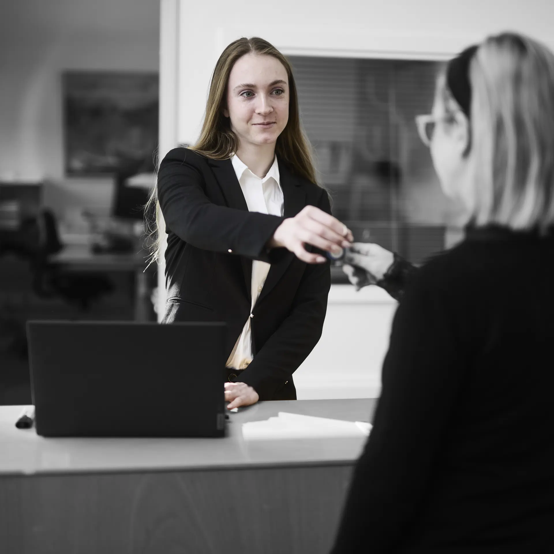 Receptionist står ved en skranke, hvor hun udleverer et sæt nøgler til kunde