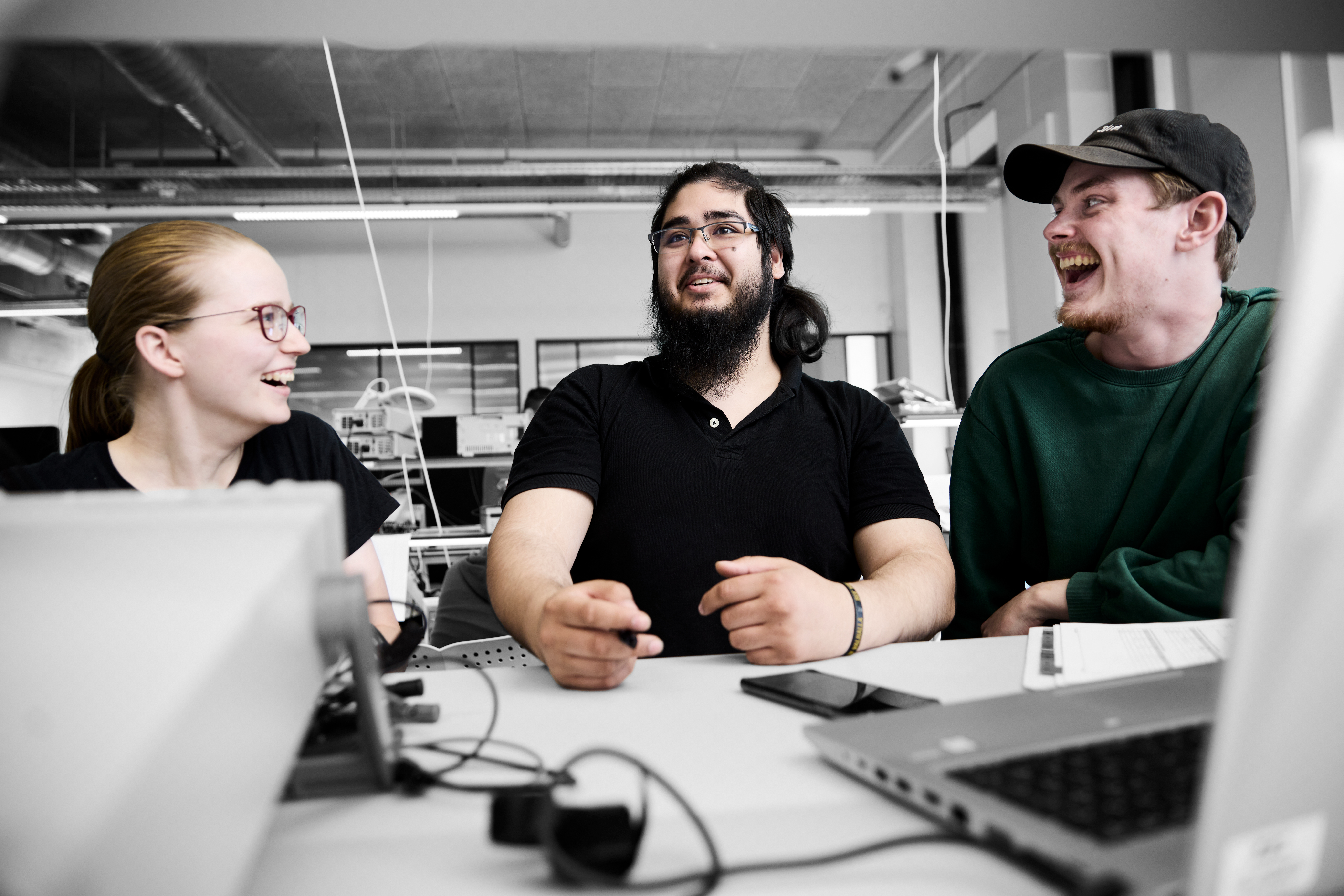 Elektronikfagteknikere arbejder ved bord og griner til hinanden