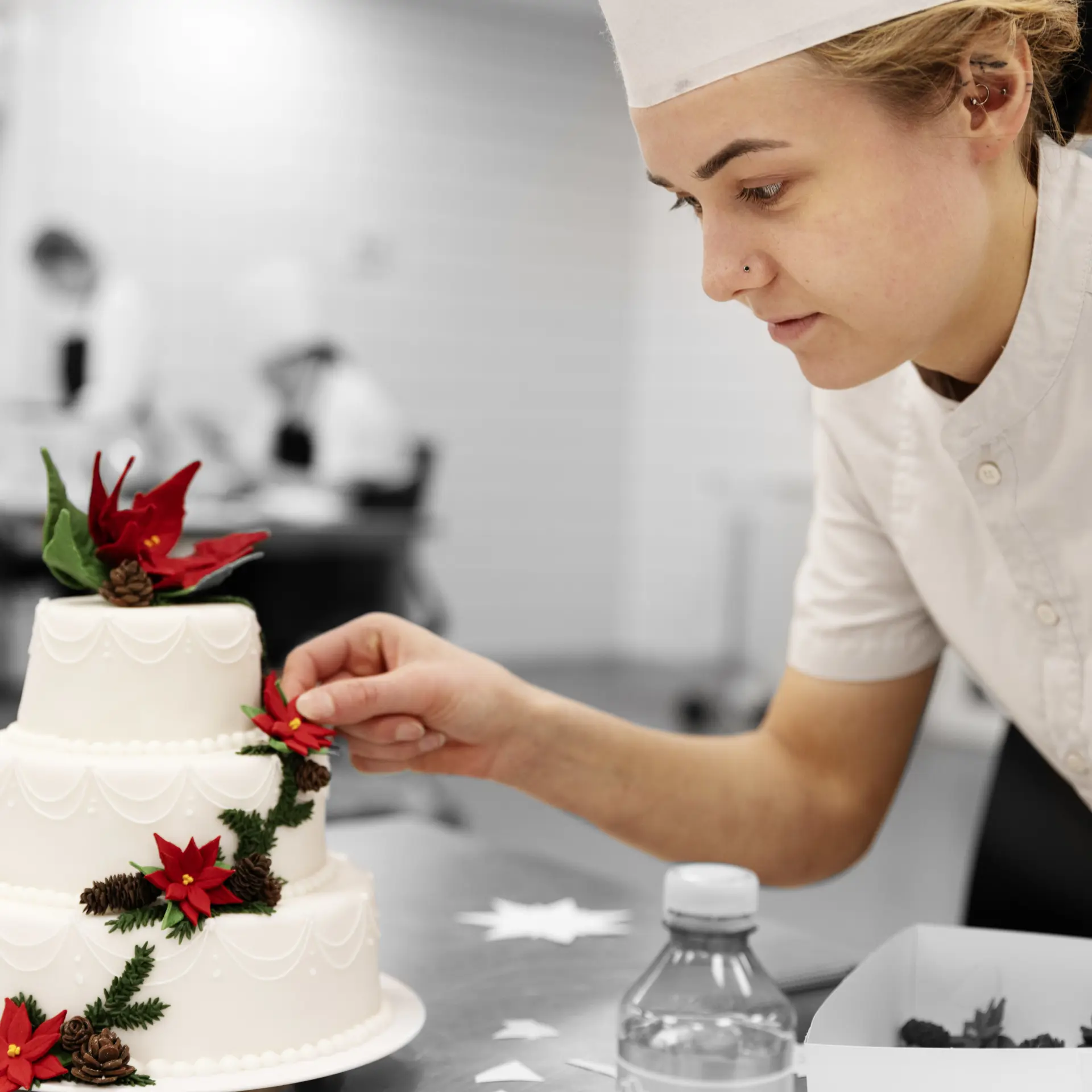 Konditor pynter en hvid bryllupskage med røde blomster