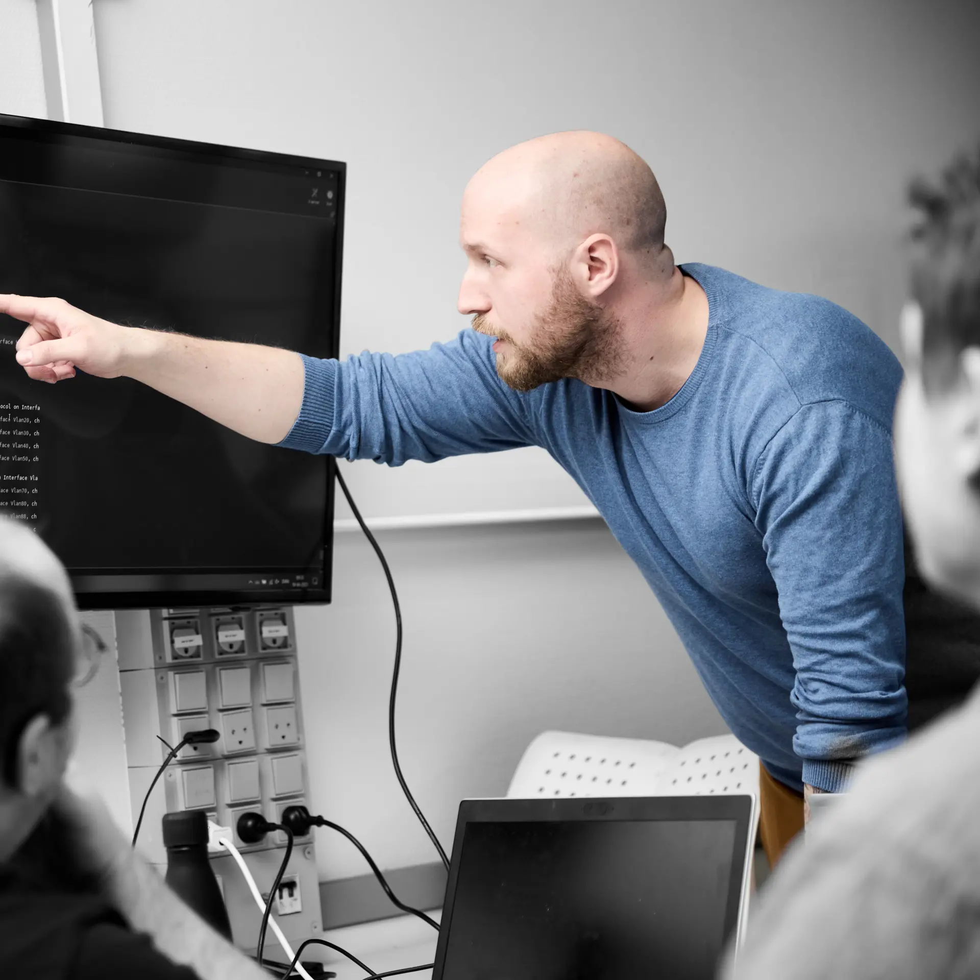Datatekniker peger på en skærm med en masse koder på, mens andre elever ser på
