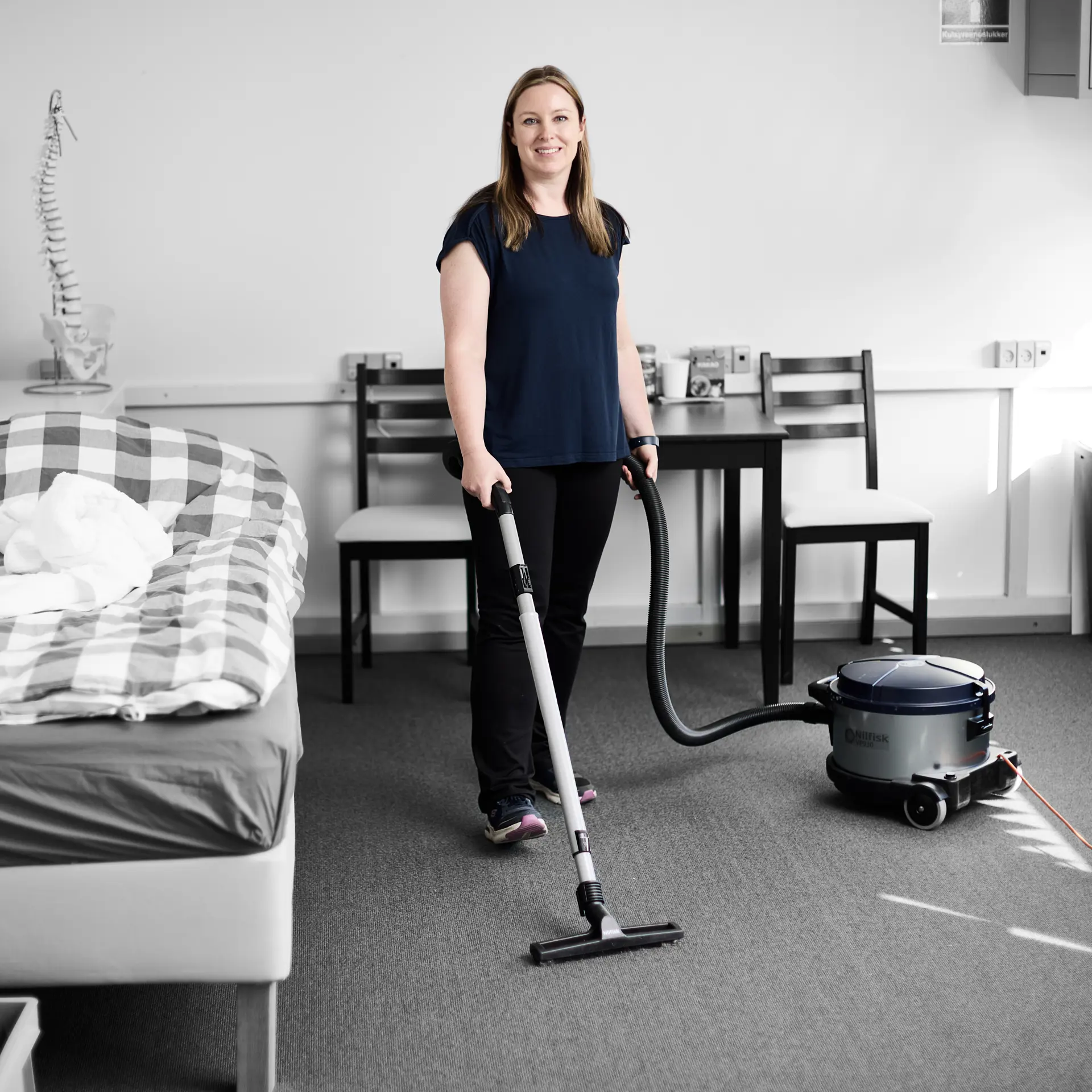 Serviceassistent smiler til kameraet, mens hun gør rent